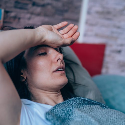 Sick young woman lying in the bed covered with blanket. Ill woman lying in bed with high temperature.